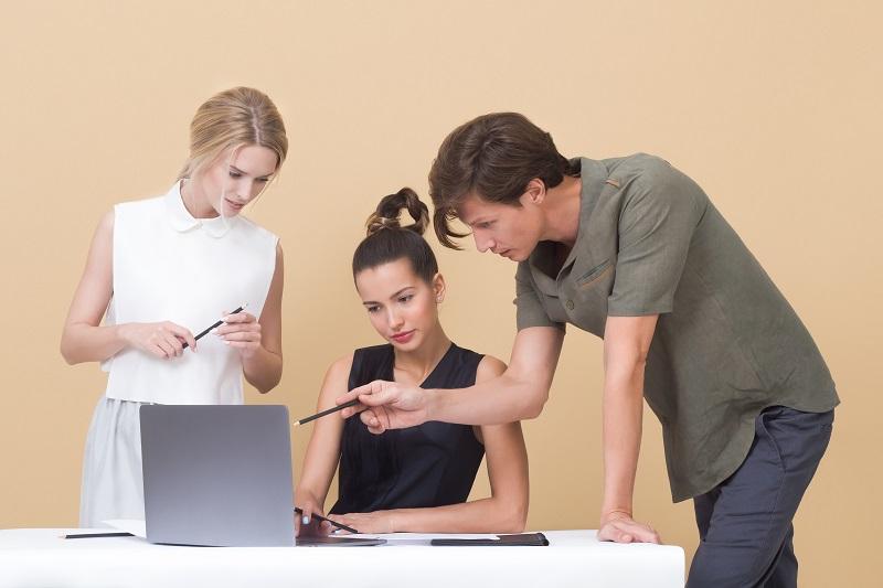Drei Mitarbeiter stehen vor einem Laptop und beraten sich zum Thema Marketing-Projektmanagement.