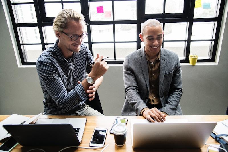 Two co-workers excitedly talking while sitting in front of their laptops.