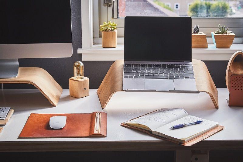 Ein Schreibtisch, auf dem sich ein Computer mit Maus und Tastatur, ein Laptop und ein Notizbuch mit Stift befinden.