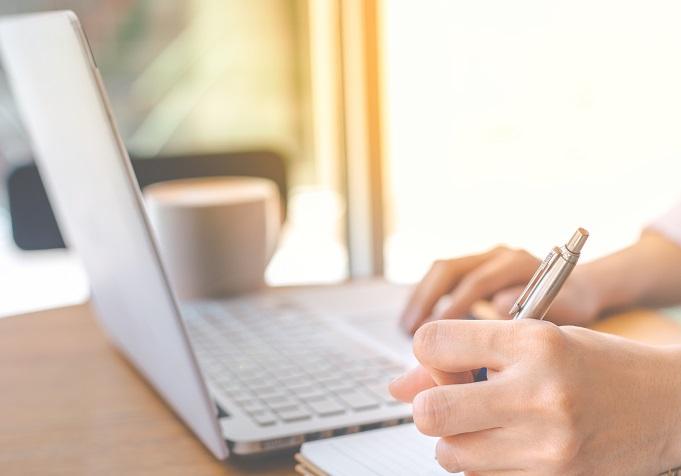Hands writing notes while on a laptop.