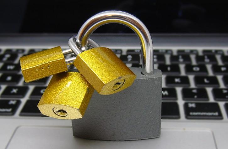 Vor einer Computertastatur steht ein größeres silbernes Vorhängeschloss, an dem sich drei kleinere goldene Vorhängeschlösser befinden.