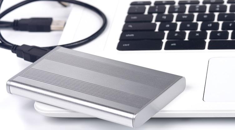 Eine mobile Festplatte liegt neben der Tastatur eines Laptop.
