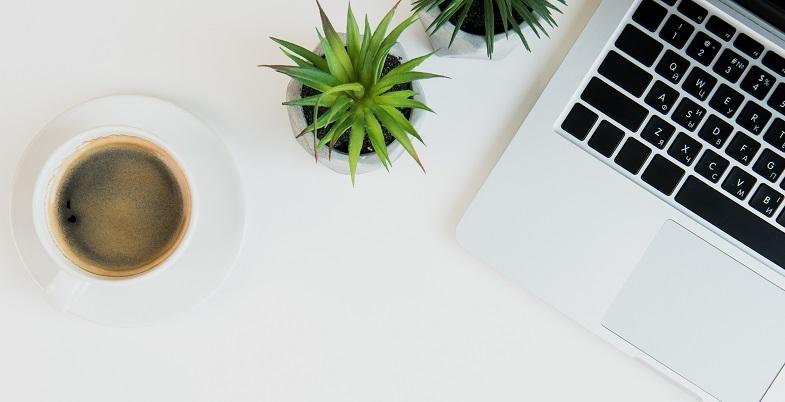 Das Bild eines Schreibtischs mit einer Tasse Kaffee, Pflanzen und einem Laptop darauf, von oben fotografiert.