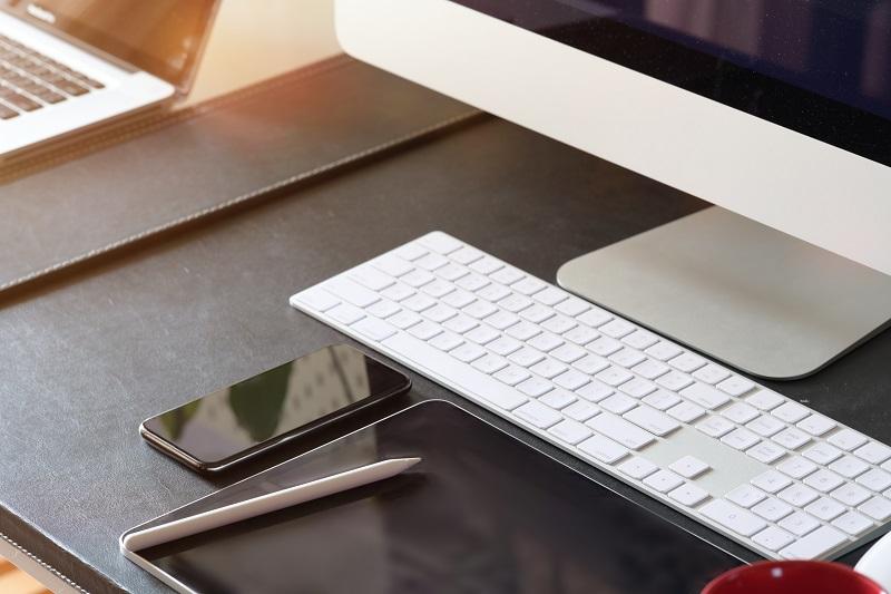 Ein Bild von einem Schreibtisch, auf dem sich ein Apple-Computer, ein Smartphone und ein Tablet-PC befinden.