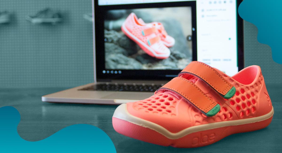 PLAE header image in blue showing a pair of childrens shoes with the digital asset of the same model being displayed on a computer screen in the background.