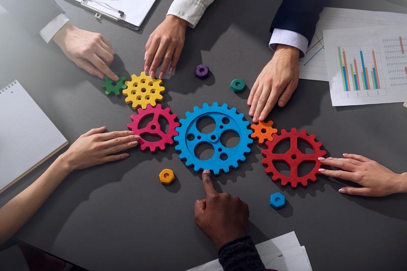 Different workers holding puzzle gears together.