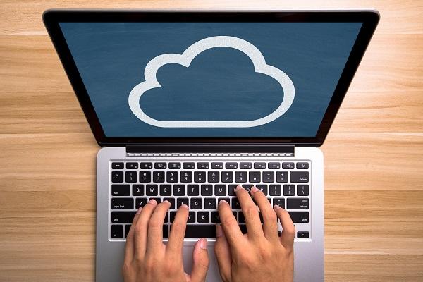 Die Hände einer Person auf der Tastatur eines Laptops, auf dessen Bildschirm ein Cloud-Symbol zu sehen ist.