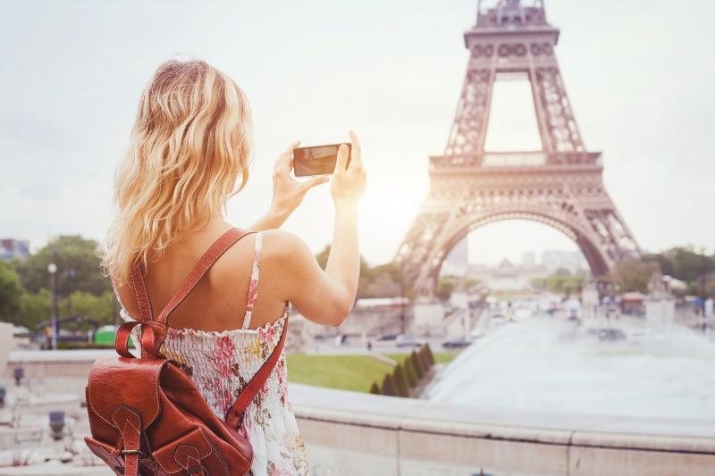 Eine junge Frau im Sommerkleid fotografiert den Eiffelturm in Paris mit ihrem Smartphone.
