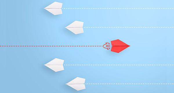 A red paper airplane flying in opposite direction of others.