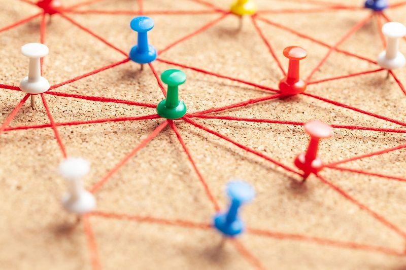 Eine Pinnwand mit Stecknadeln, die mit Fäden untereinander verbunden sind und ein Netzwerk symbolisieren.