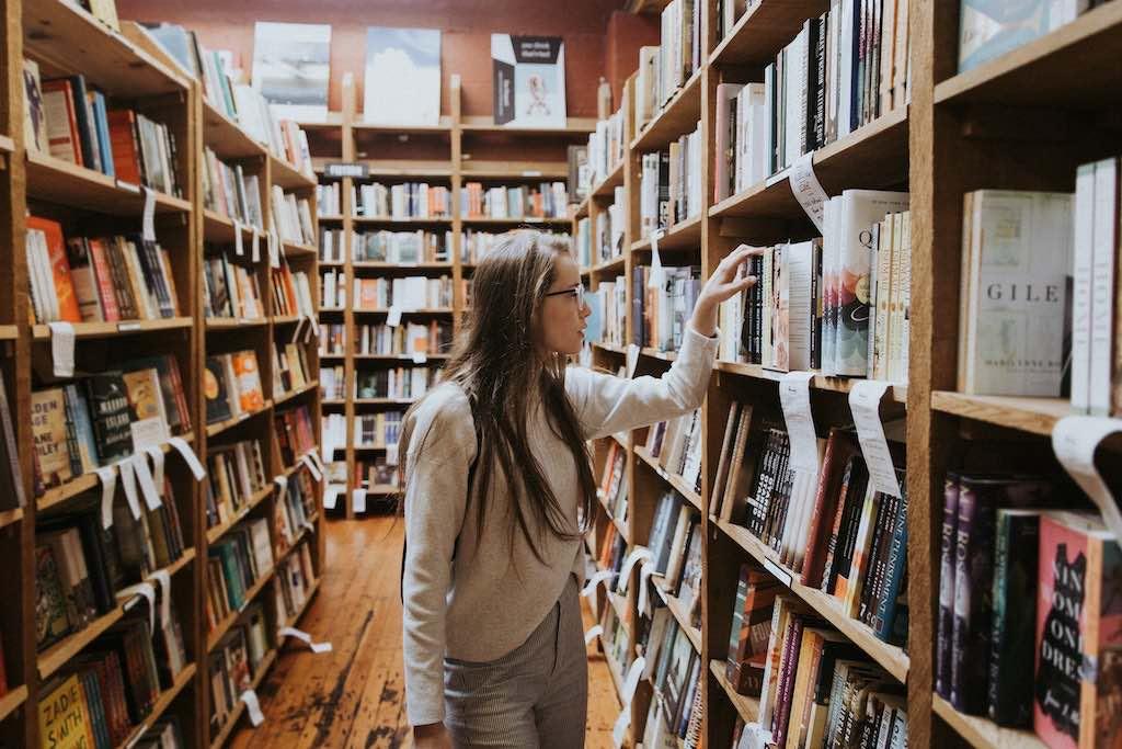 Eine junge Studentin betrachtet die Bücher in den vollen Regalen einer Bibliothek.