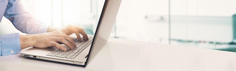 Ein Geschäftsmann tippt auf einem Laptop, während er an einem Schreibtisch sitzt.