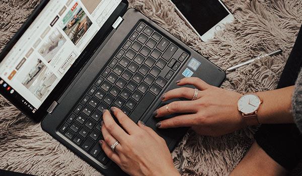 A person typing a blog on a laptop on a bed.