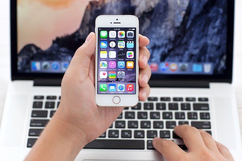 Eine Person bedient mit einer Hand ein Mobiltelefon und mit der anderen Hand einen Laptop.