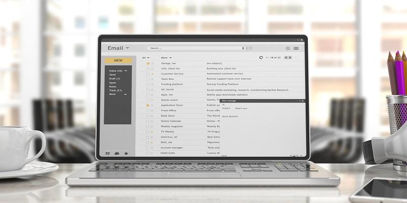 Auf einem Schreibtisch in einem Büro steht ein Laptop, auf dessen Bildschirm ein E-Mail-Programm angezeigt werden.