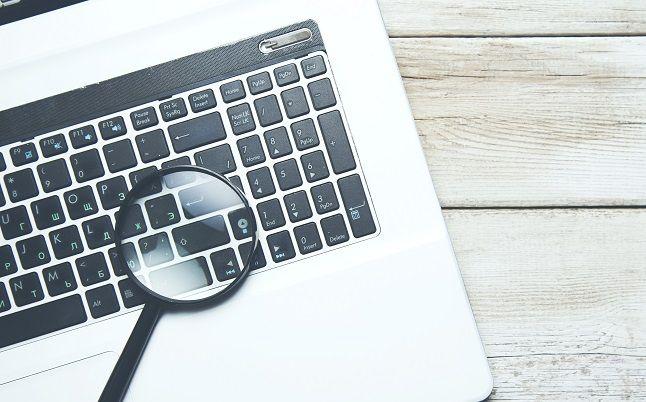 Ein Laptop, auf dessen Tastatur ein Vergrößerungsglas liegt.