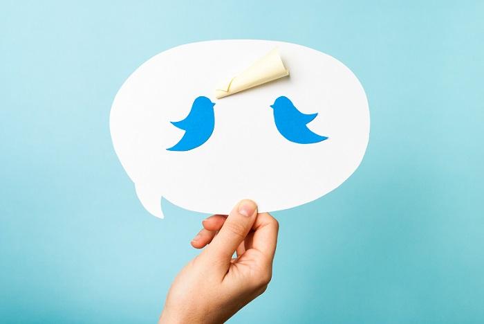 Abbildung einer Hand, die eine Sprechblase mit einer nachricht und dem zweifachen blauen Vogelsymbol von Twitter hochhält.