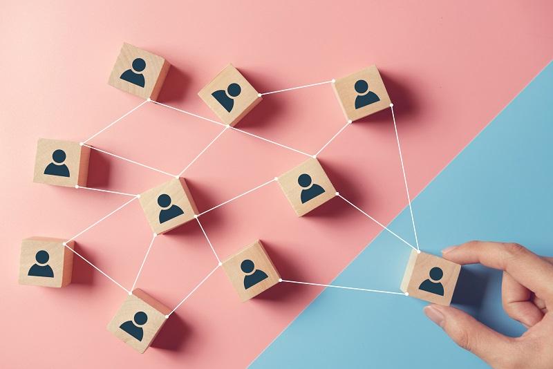 Eine Gruppe von Holzklötzen, die Personen symbolisieren, und die mit Fäden verbunden sind, was ein Netzwerk wie beim Co-Branding darstellt.