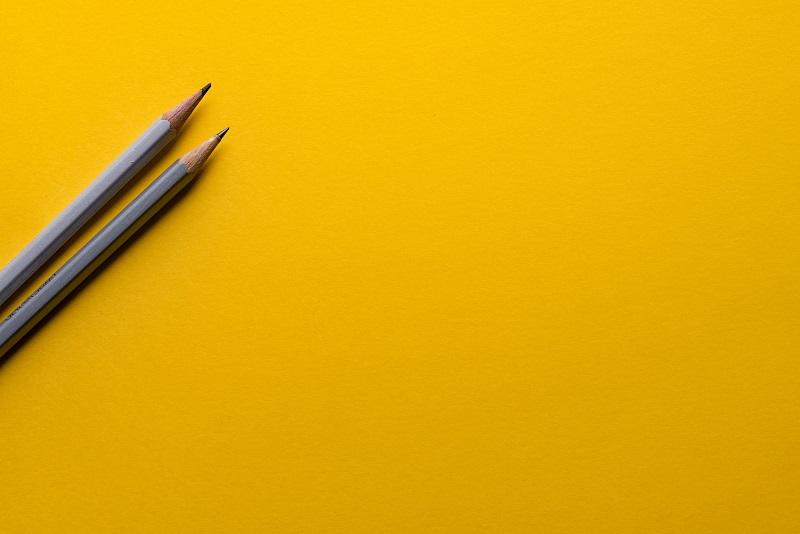 Ein gelber Hintergrund, auf dem zwei Bleistifte liegen.