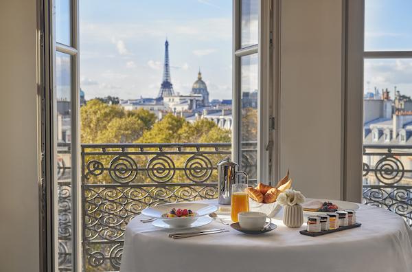 A breakfast table set in front of an open window with the Eiffel tower in Paris in the back.