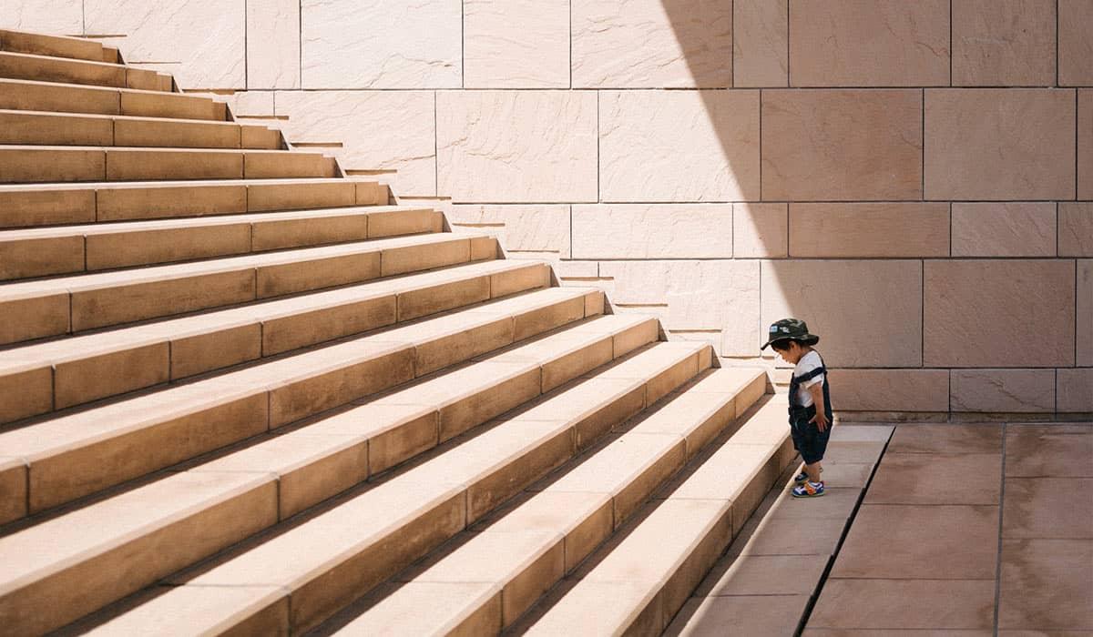 Ein kleines Kind steht vor der ersten Stufe einer Treppe.