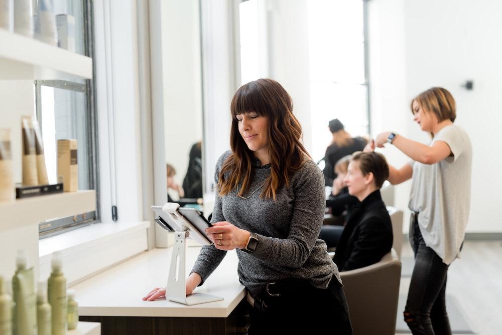 Salon owner using an iPad with hair stylists working in the background.