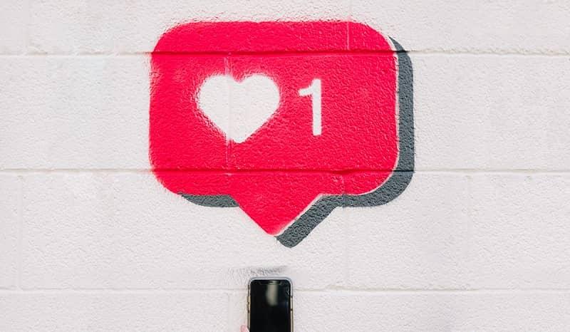 Ein Smartphone unter einer Wandbemalung in Form eines Herzens mit einer 1 als Symbol für ‘Gefällt mir’.