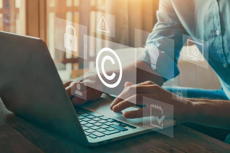 Eine Person sitzt an einem Laptop, vor ihr schweben Warnsymbole und Copyright-Zeichen.