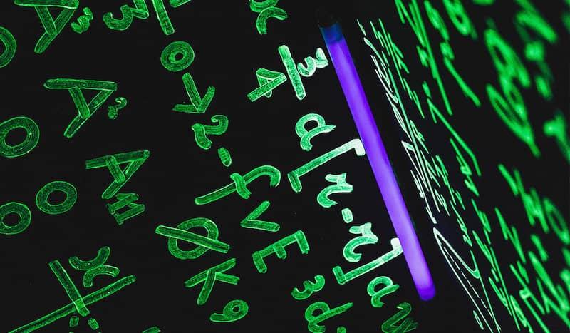 Mathematische Formeln wurden mit fluoreszierender Farbe an eine Tafel geschrieben und leuchten unter einem Schwarzlicht auf.