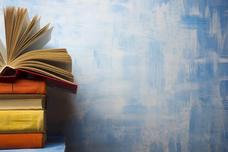 Auf einem Holztisch liegt ein Stapel gebundener Bücher, bei dem das oberste Buch aufgeschlagen ist.