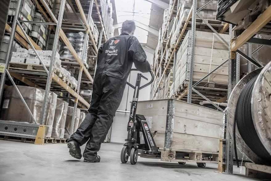 Screenshot eines Assets von Logitrans in Canto, in dem eine Person im Overall einen beladenen Wagen durch das Lagerhaus schiebt.