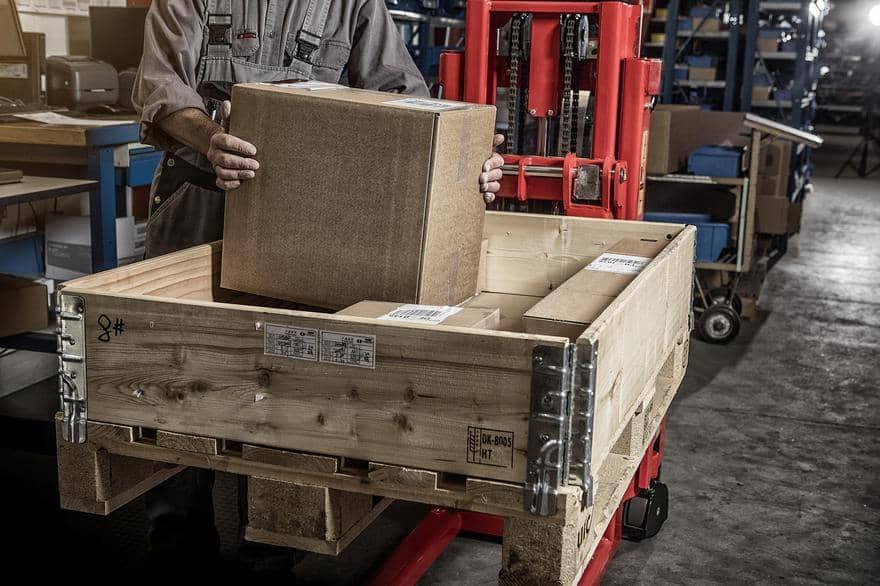 Screenshot eines Assets von Logitrans in Canto, in dem eine Person zu sehen ist, die in einem Lagerhaus einen Holzwagen mit Pappkartons belädt.