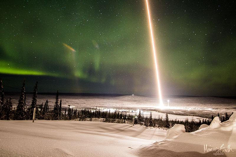 Swedish Space Corporation SPIDER 2 sounding rocket launch from Esrange Space Center, February 2020. Credit for the image goes to Marcus Lindh, SSC. The image shows a snowy, forest-covered hilltop with a bright red laser-type light shooting straight into the sky at a slight left angle. The sky is a slightly green-black.