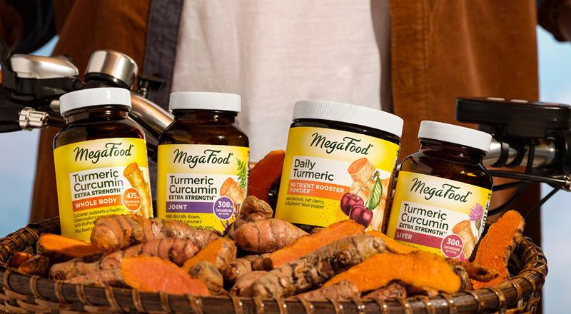 a zoomed in shot of the basket of a man on a bike, the basket holds MegaFood brand supplements and vitamins with turmeric roots around over a light blue background