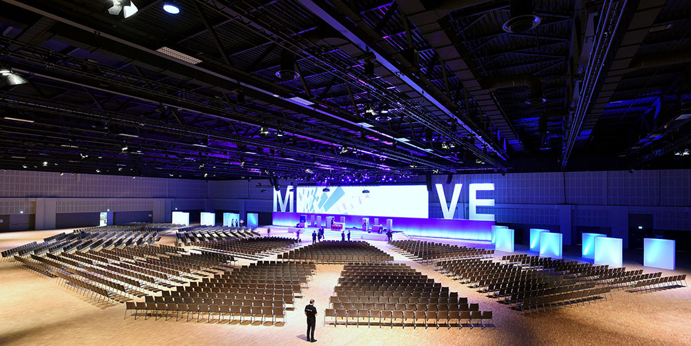 The connected conference and convention center for conferences and events. Large auditorium with auditorium style seating and stage with large screen/letters: MVE and blue lighting