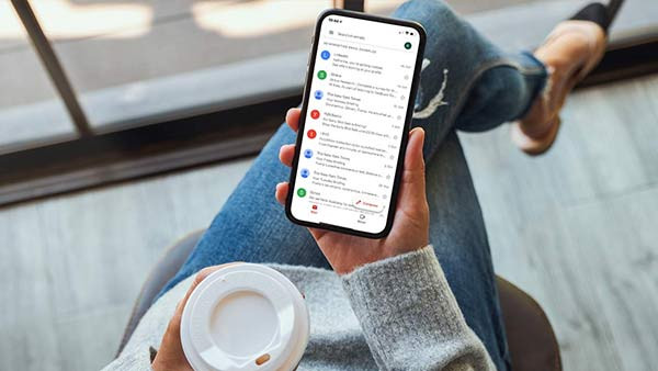 Woman holding smartphone with email inbox on screen.