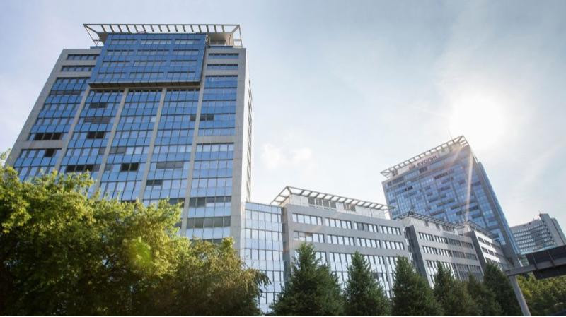 An image of Evonik Center Campus in Essen, large glass building connected to other large buildings with loads of windows, and trees in the foreground