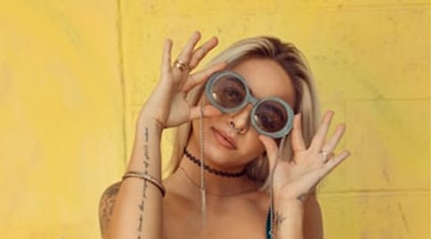Woman in round glasses against a yellow wall